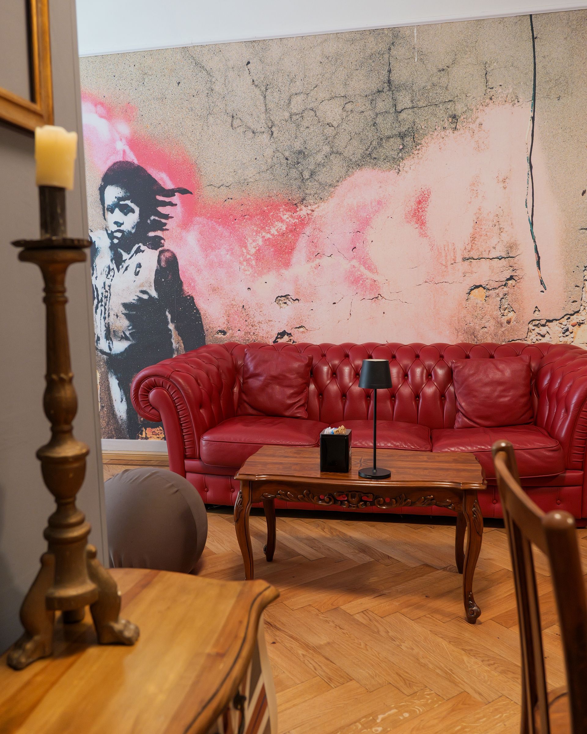 Soggiorno con divano in pelle rossa, tavolo in legno e murale di Banksy.
