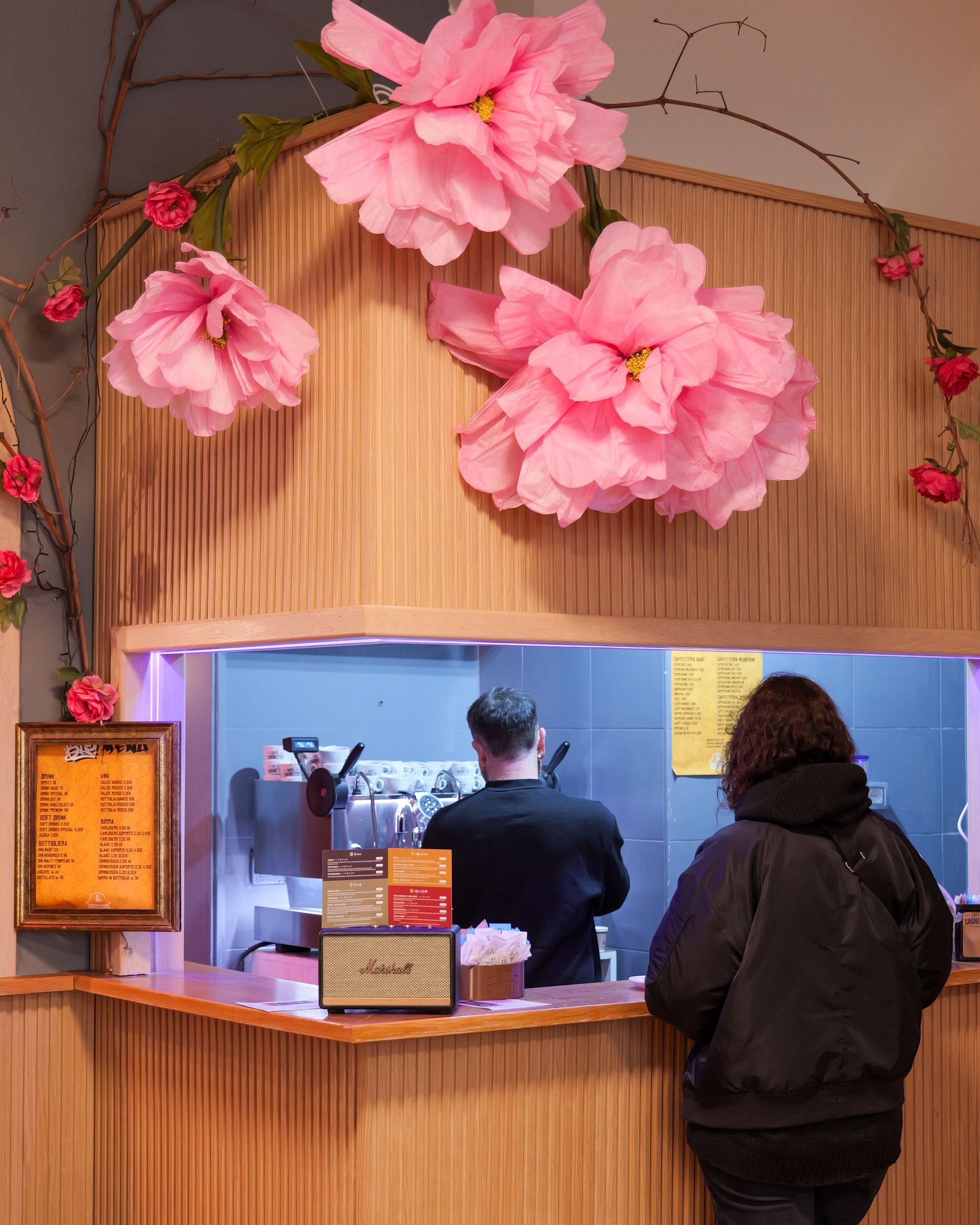 Fiori di carta rosa decorano un bancone del cibo; una persona ordina da un dipendente.