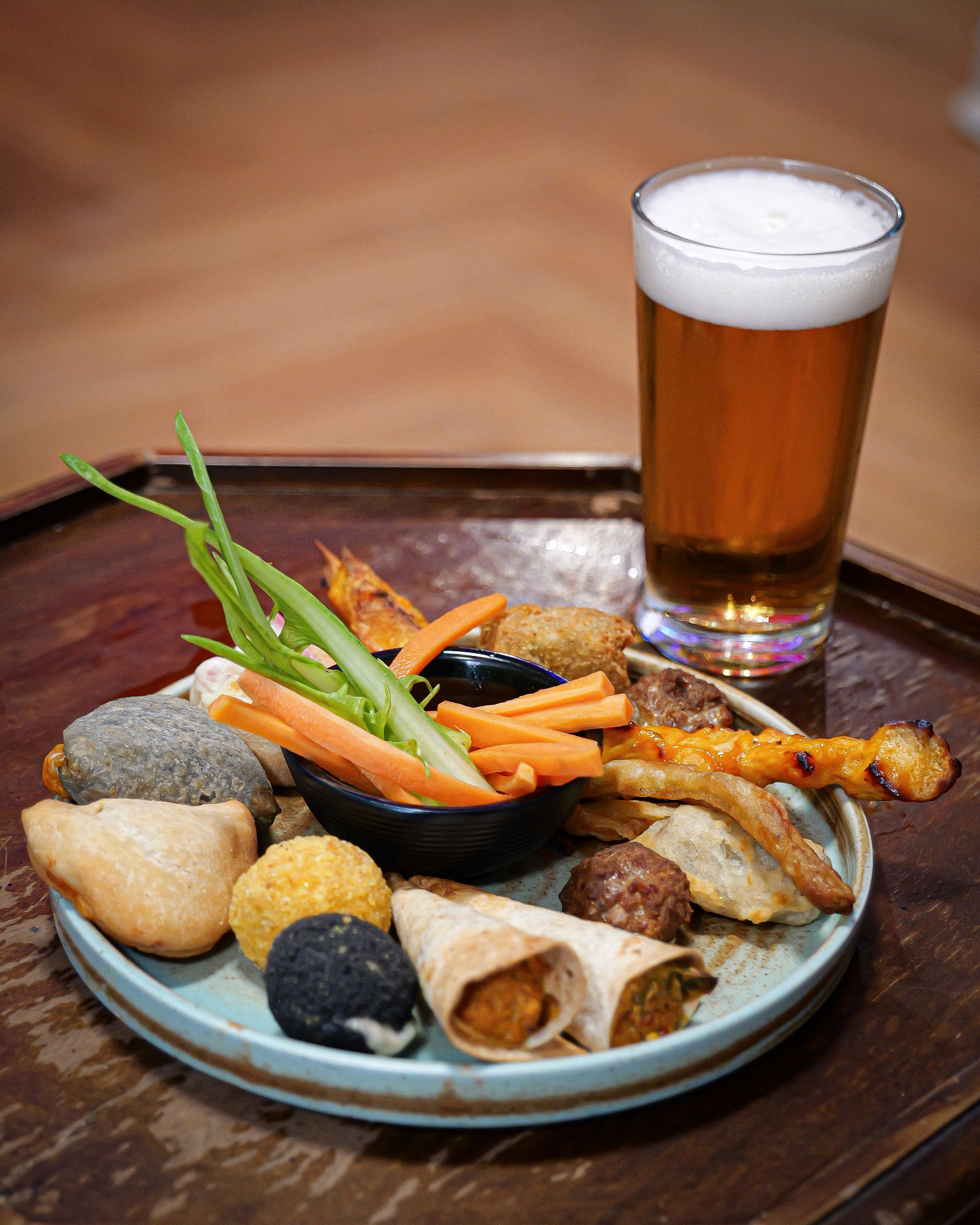 Piatto di antipasti assortiti con una birra su un vassoio.