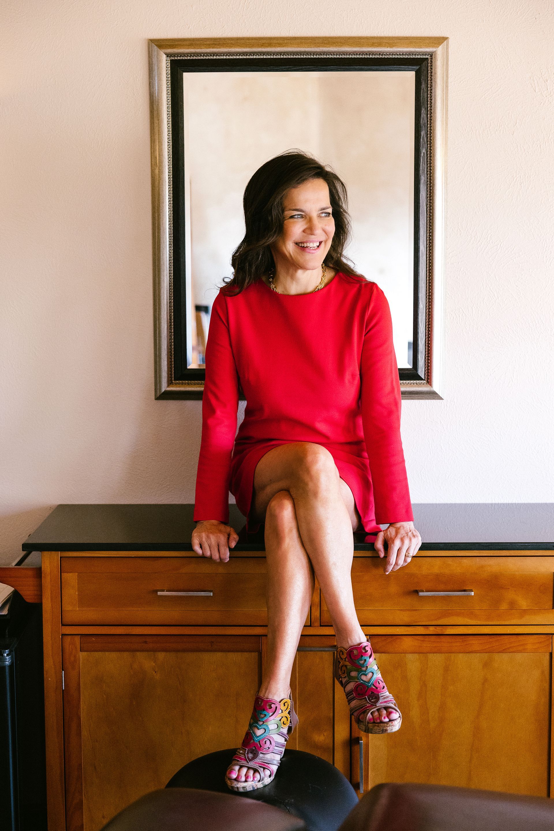 A woman wearing a red jacket and hoop earrings smiles for the camera.