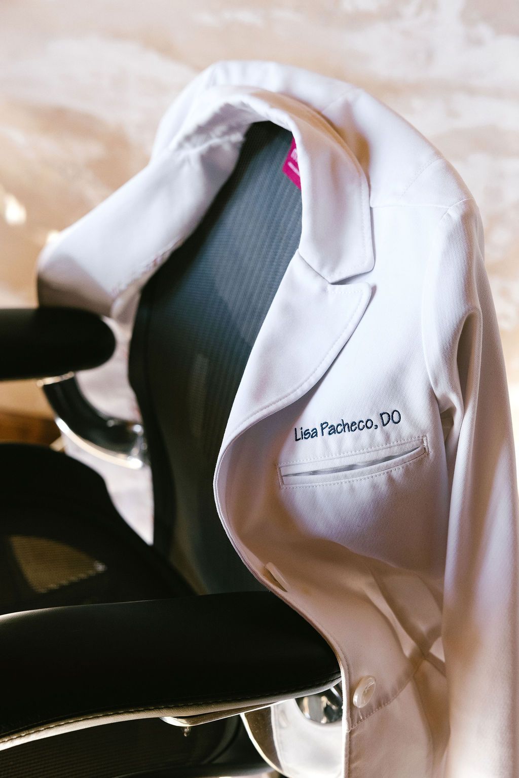 White lab coat draped on a chair with the name Lisa Rizzuto, DO, visible.