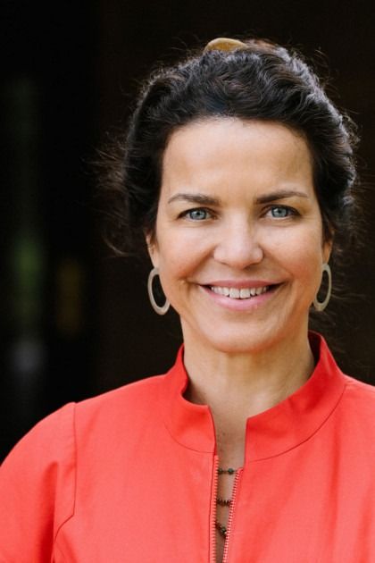 A woman wearing a red jacket and hoop earrings smiles for the camera.