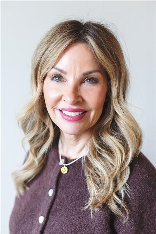 A woman wearing a blue turtleneck and a necklace is smiling for the camera.