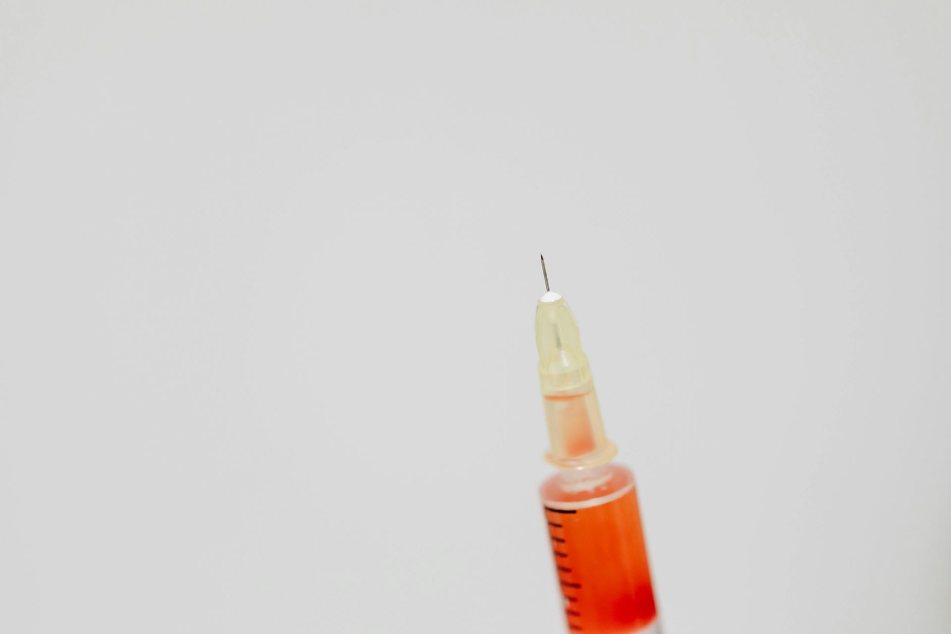 A close up of a syringe with red liquid in it on a white background.