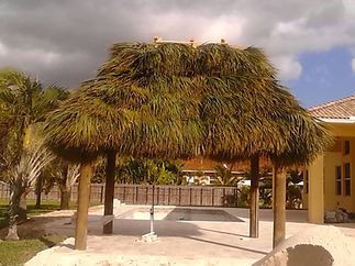 A thatched gazebo with a swimming pool in the background.