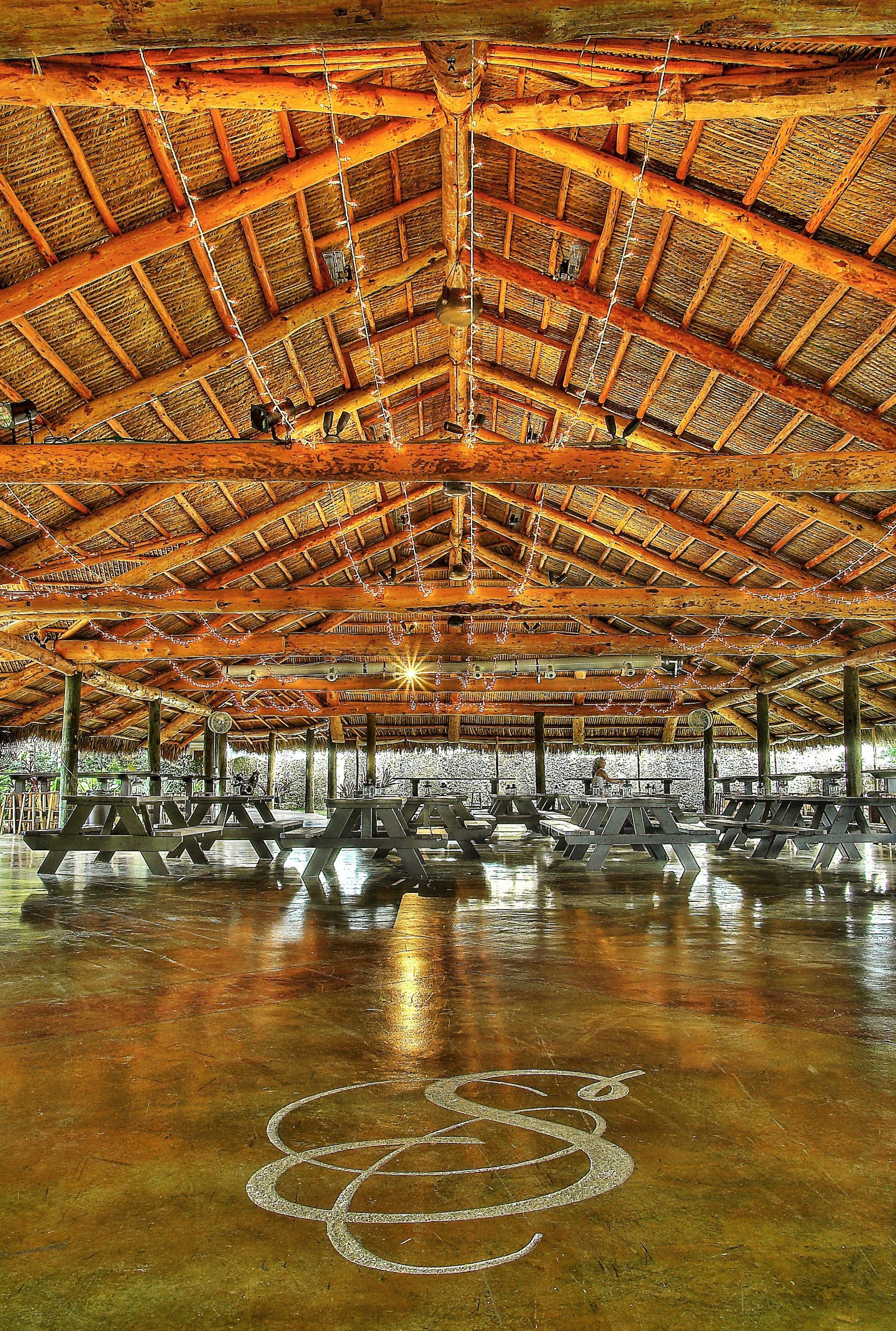 A large room with a thatched roof and a reflection of the ceiling in the floor.