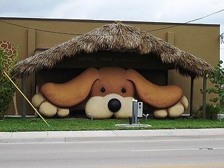A statue of a dog is sitting under a thatched roof.