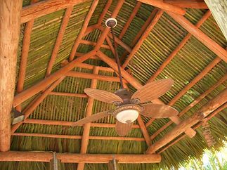 A ceiling fan is hanging from the ceiling of a thatched roof.