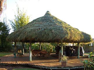 A thatched gazebo with a wooden deck and chairs underneath it.