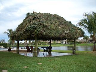 A thatched gazebo with a table and chairs in front of a body of water