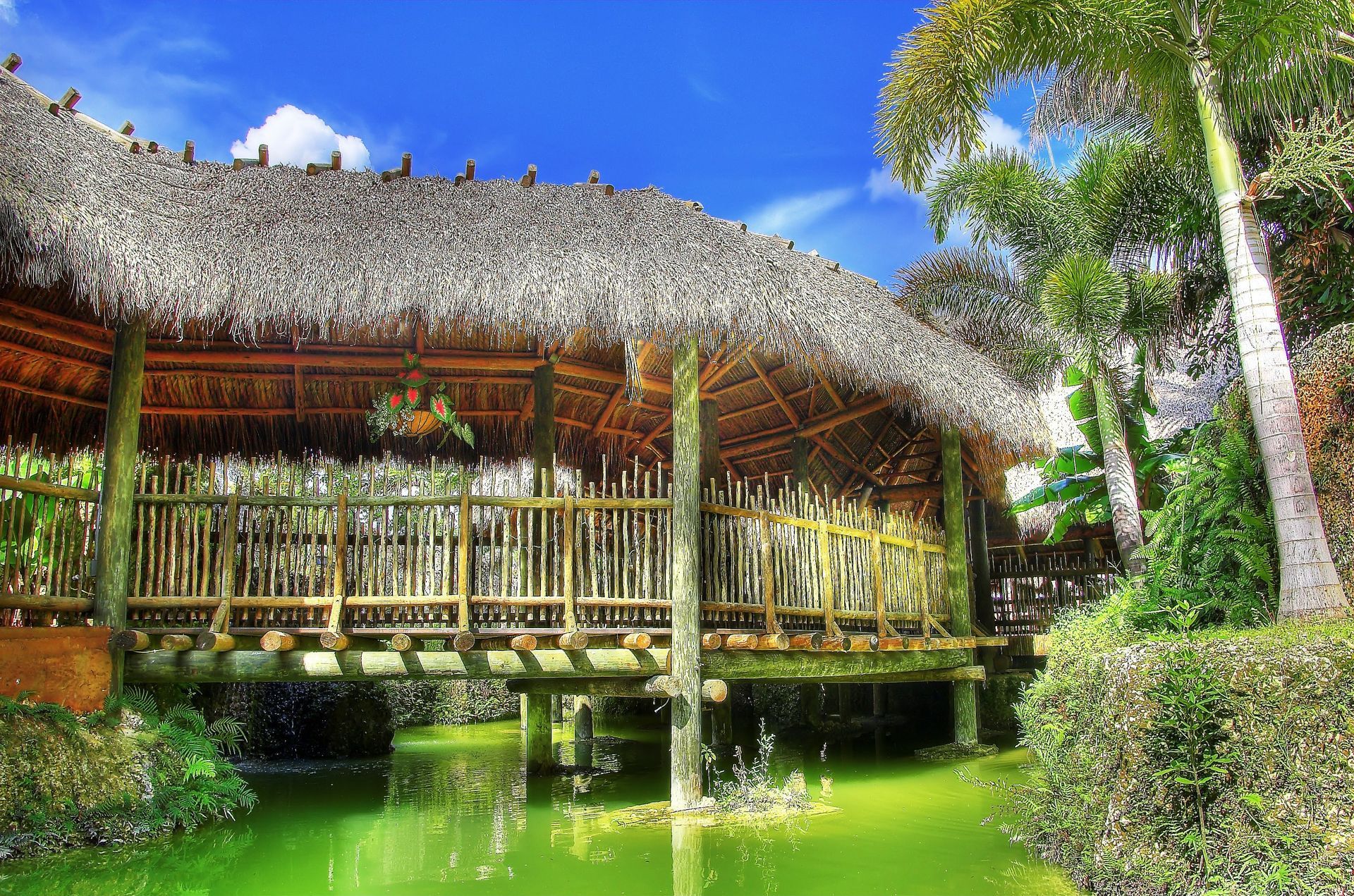 A wooden bridge over a pond with a thatched roof