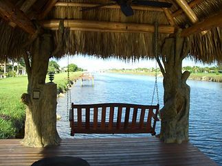 A thatched gazebo with a swing overlooking a body of water