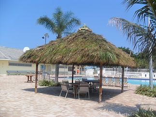 A thatched gazebo with a table and chairs in front of a swimming pool.