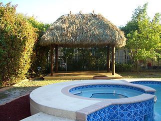 A hot tub with a thatched roof next to a swimming pool