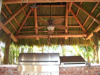 A grill under a thatched roof with a ceiling fan