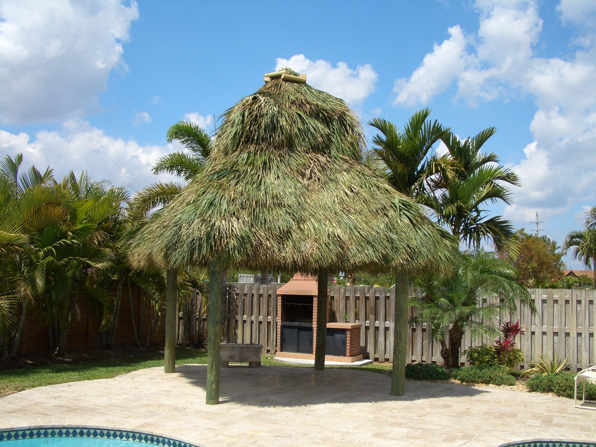 A gazebo with a thatched roof sits next to a pool