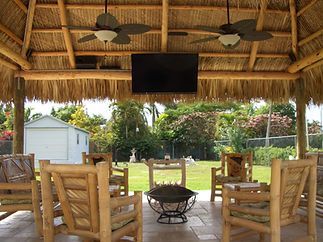 A thatched gazebo with chairs and a flat screen tv