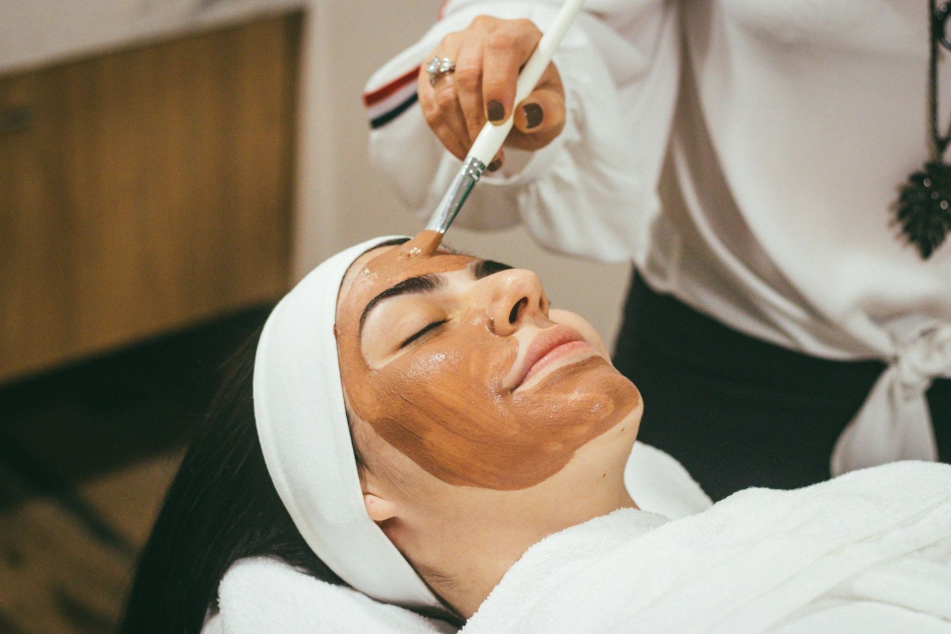 Woman receiving facial mask application at a spa.