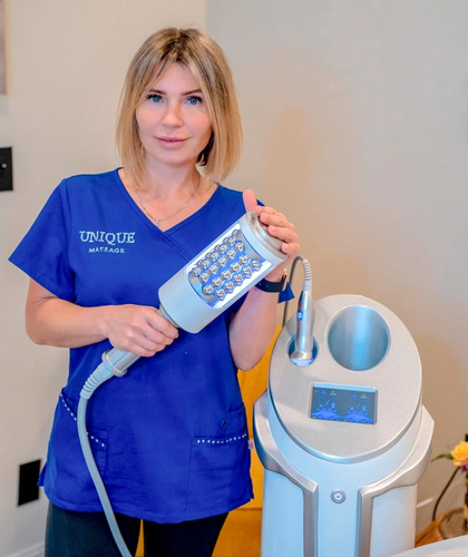 Woman in blue scrubs holding a medical device with a light head, next to a silver machine.