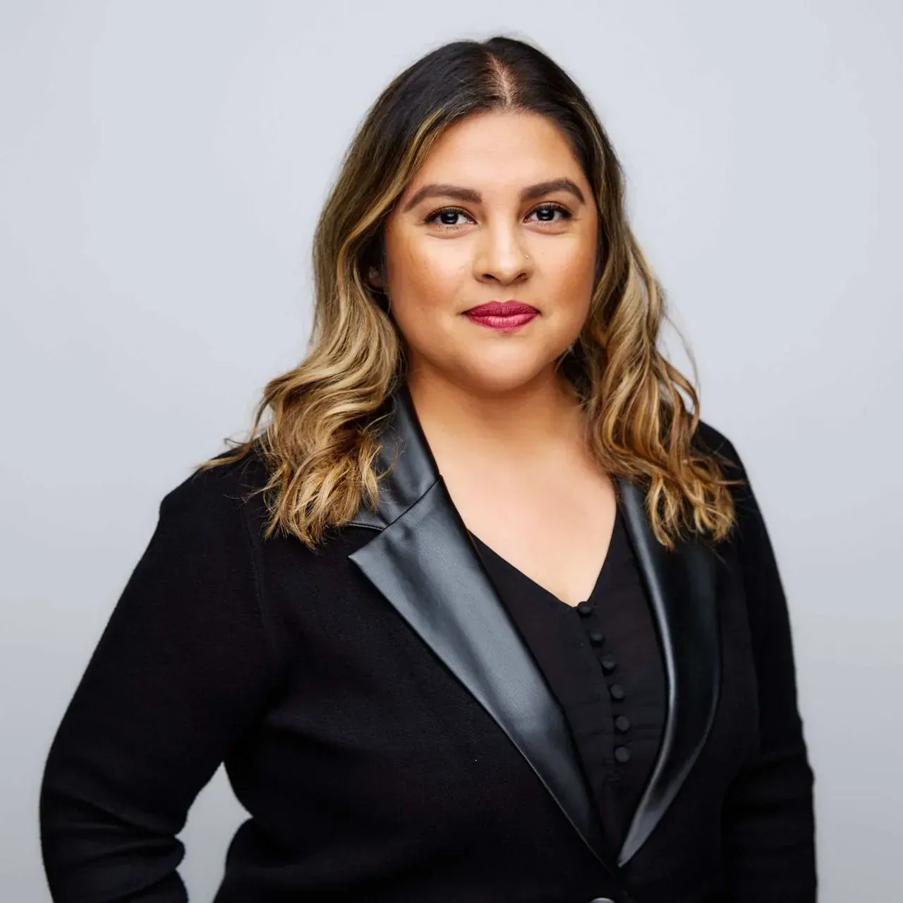 Woman with dark hair and a black jacket smiles at the camera.