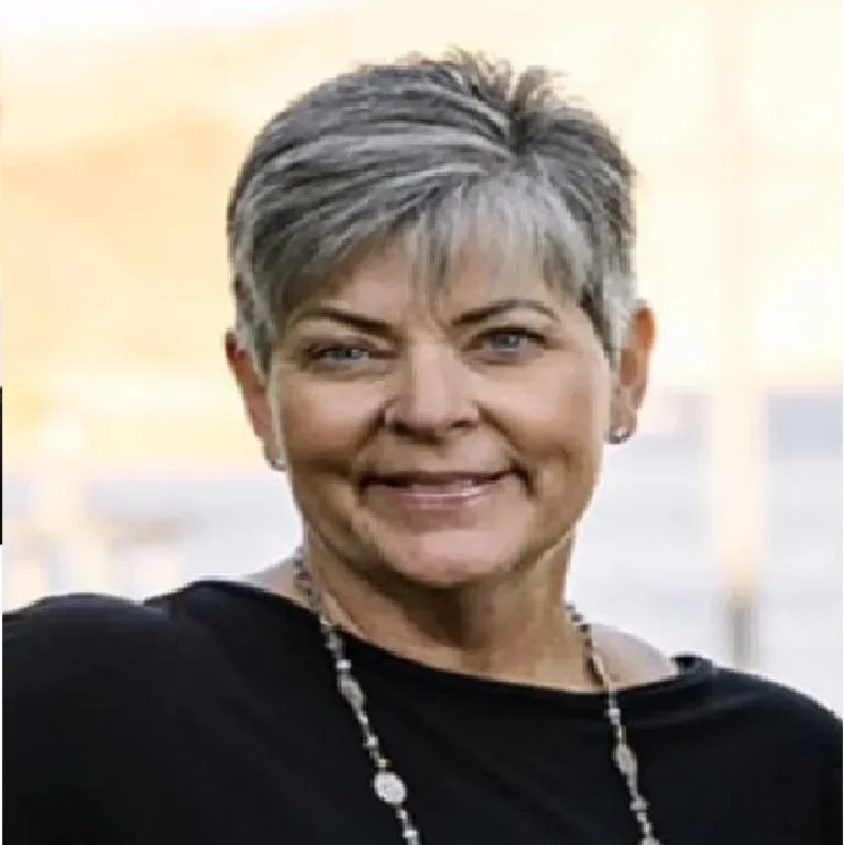 Smiling woman with short gray hair, wearing a black top and necklace; outdoors.