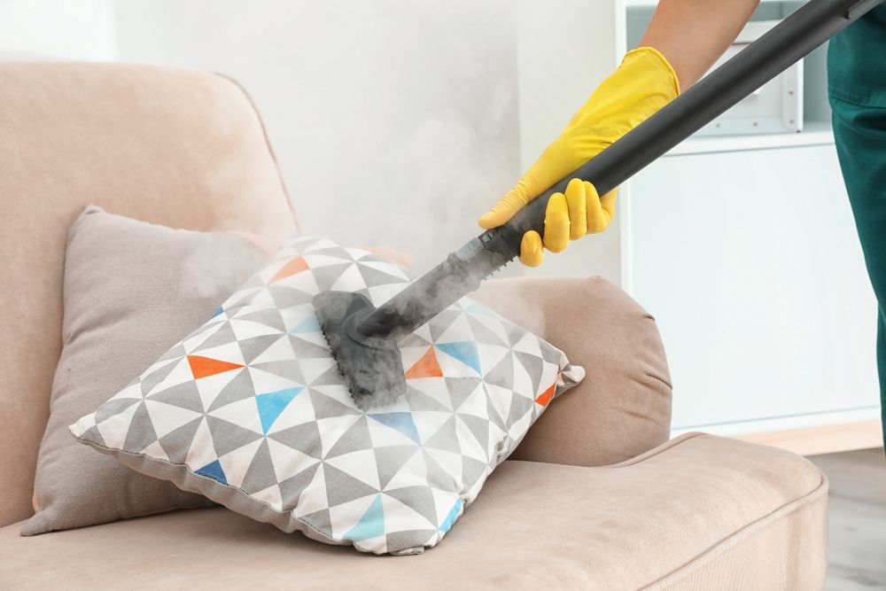 Person Steam Cleaning a Patterned Pillow on a Beige Sofa; Steam Visible — Clean Coast Carpet Cleaning in Port Stephens, NSW