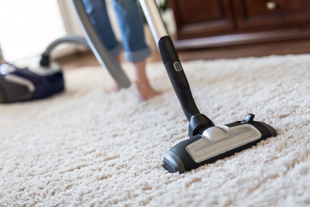 Person Vacuuming a White Carpet in a Room With Wood Furniture — Clean Coast Carpet Cleaning in Port Stephens, NSW