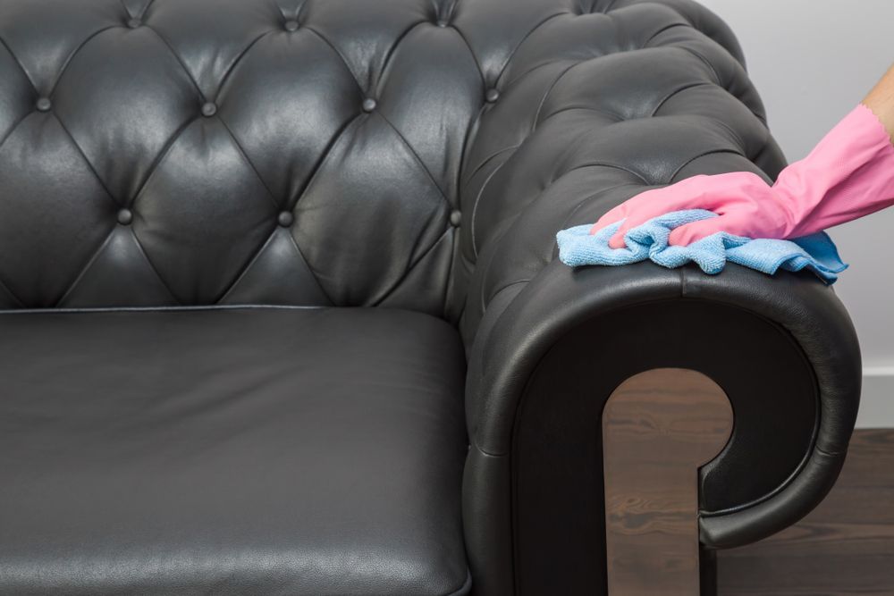 Person in Pink Gloves Wiping a Black Leather Tufted Sofa — Clean Coast Carpet Cleaning in Port Stephens, NSW