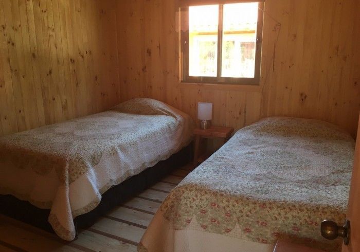Pequeña habitación de madera con dos camas individuales y una ventana entre ellas.