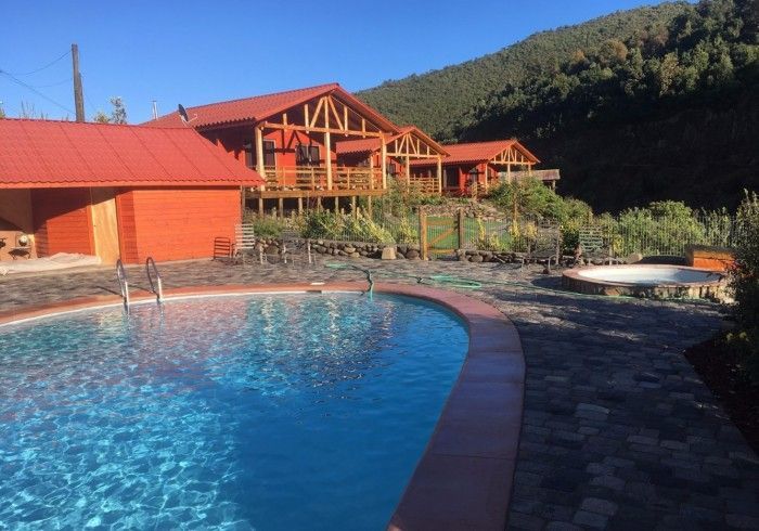 Piscina azul junto a cabañas de madera con techos rojos en un soleado complejo de montaña.