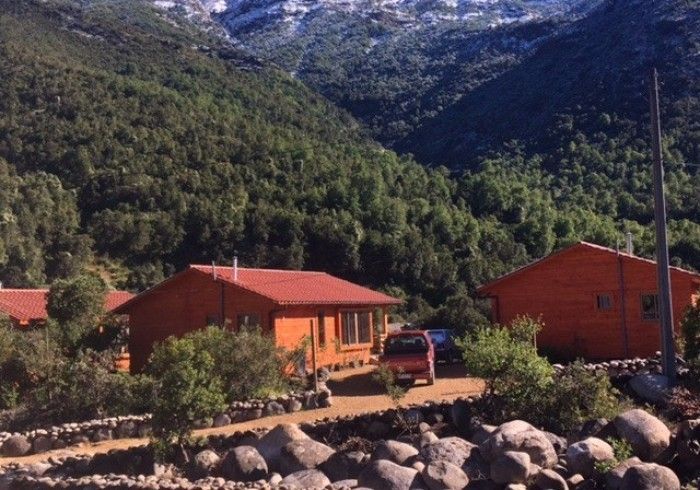 Cabañas con techos rojos en un valle de montaña con rocas y árboles en primer plano.