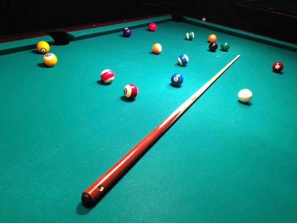 A pool table with balls and a cue on it