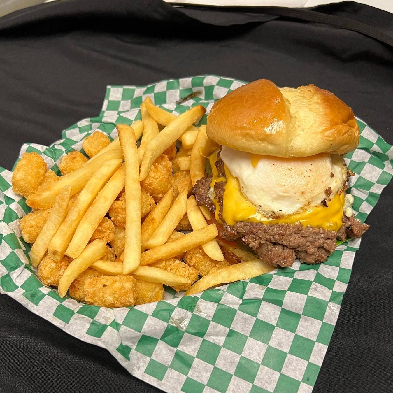 A hamburger and french fries on a green checkered paper on a table.