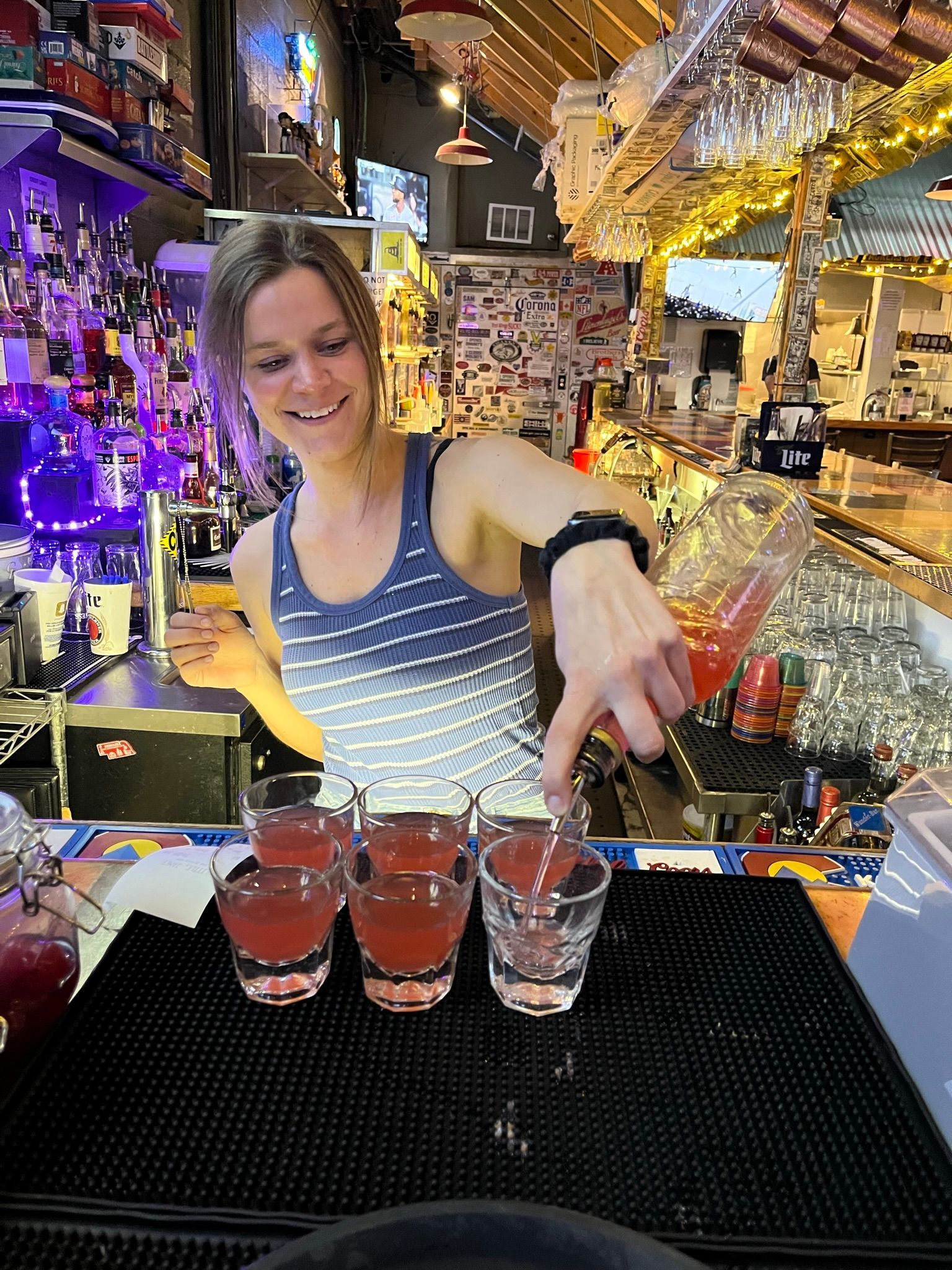 A woman is pouring a drink into a shot glass at a bar.