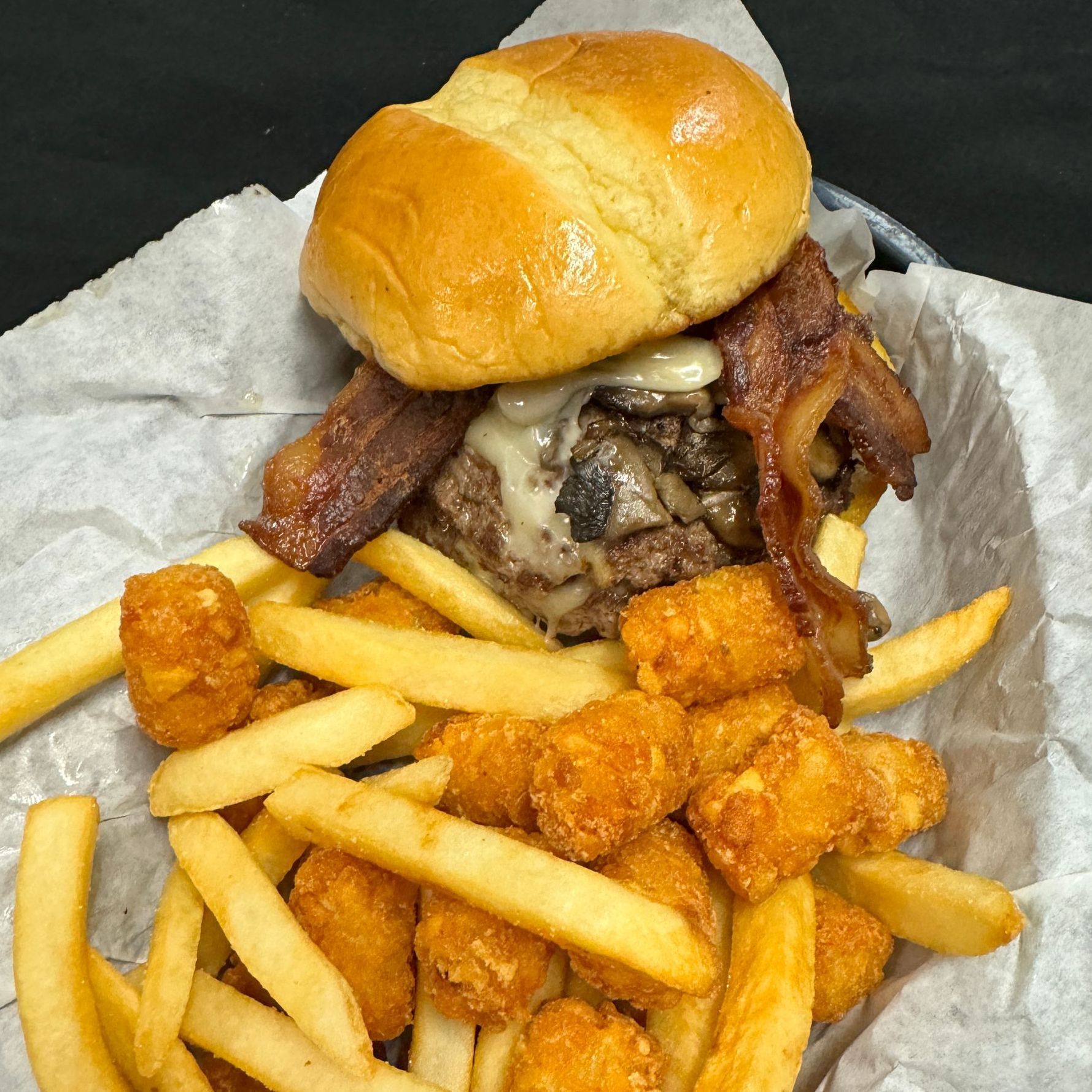 A hamburger with french fries and tots on a bun