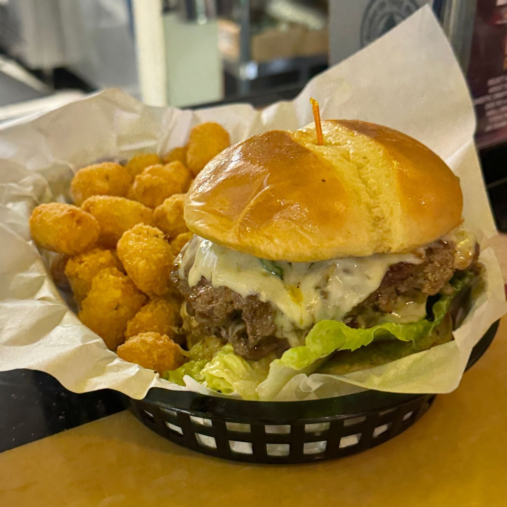 A hamburger and tots in a basket on a table.