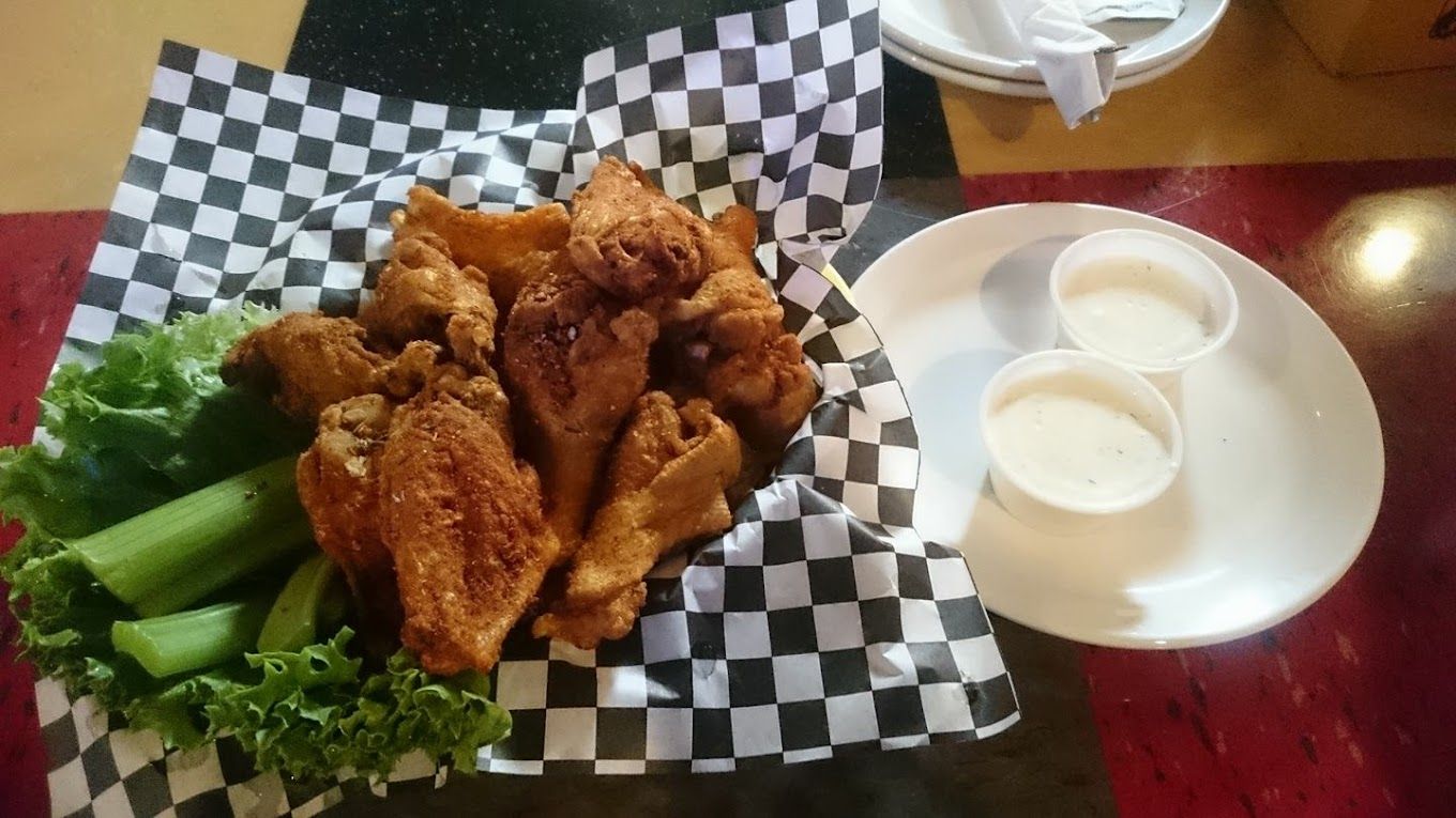 A basket of fried chicken wings with lettuce and dipping sauce on a table.