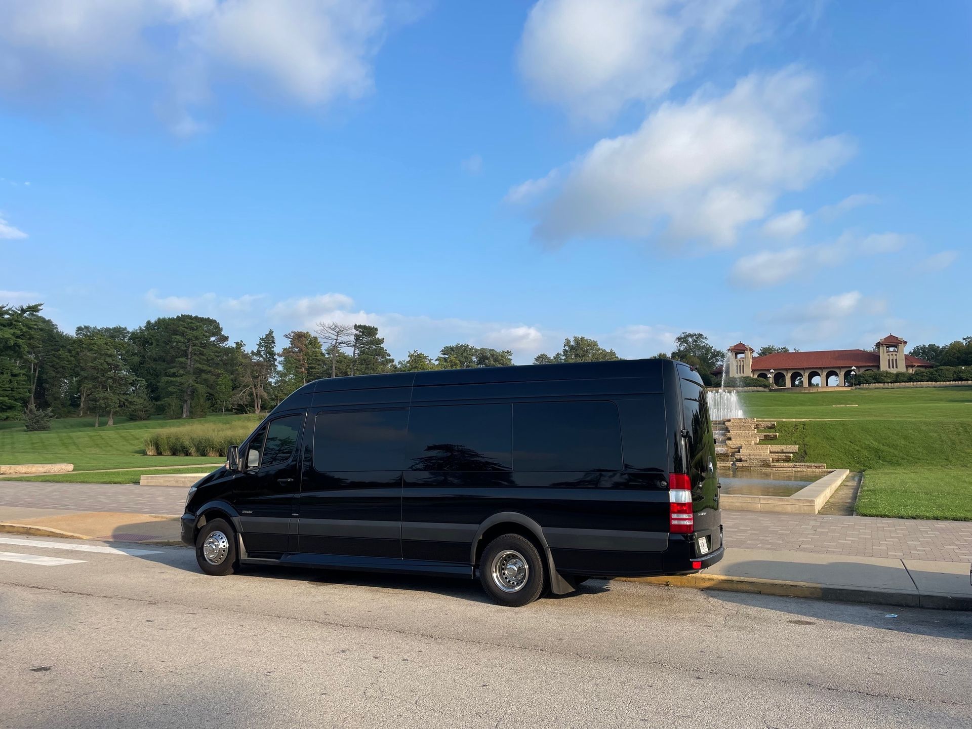 A black van is parked on the side of the road in front of a golf course.