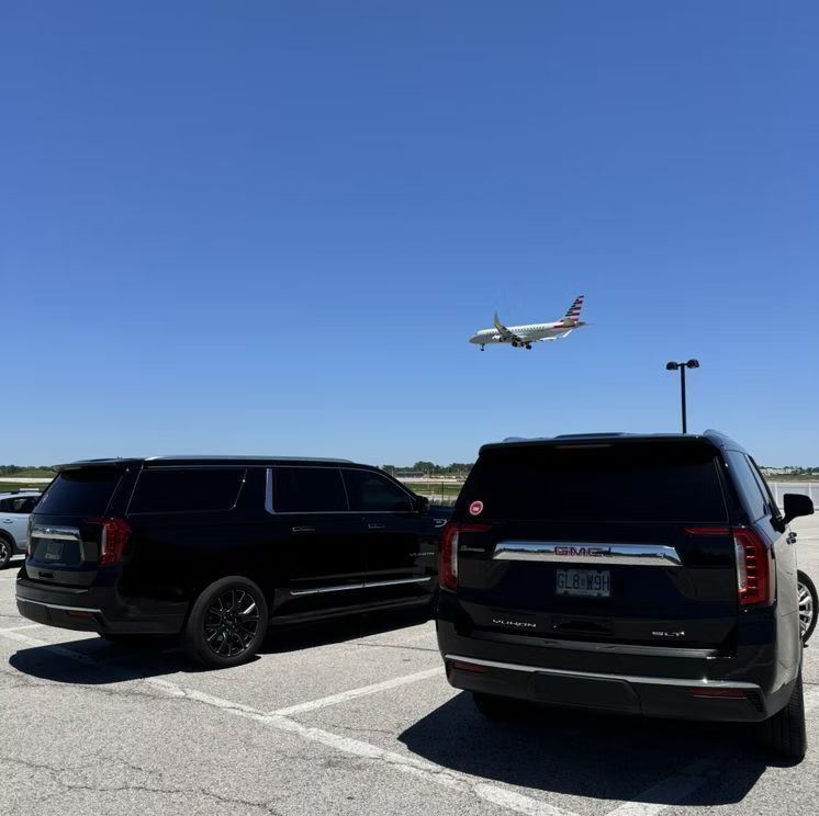 A plane is flying over two cars parked in a parking lot.