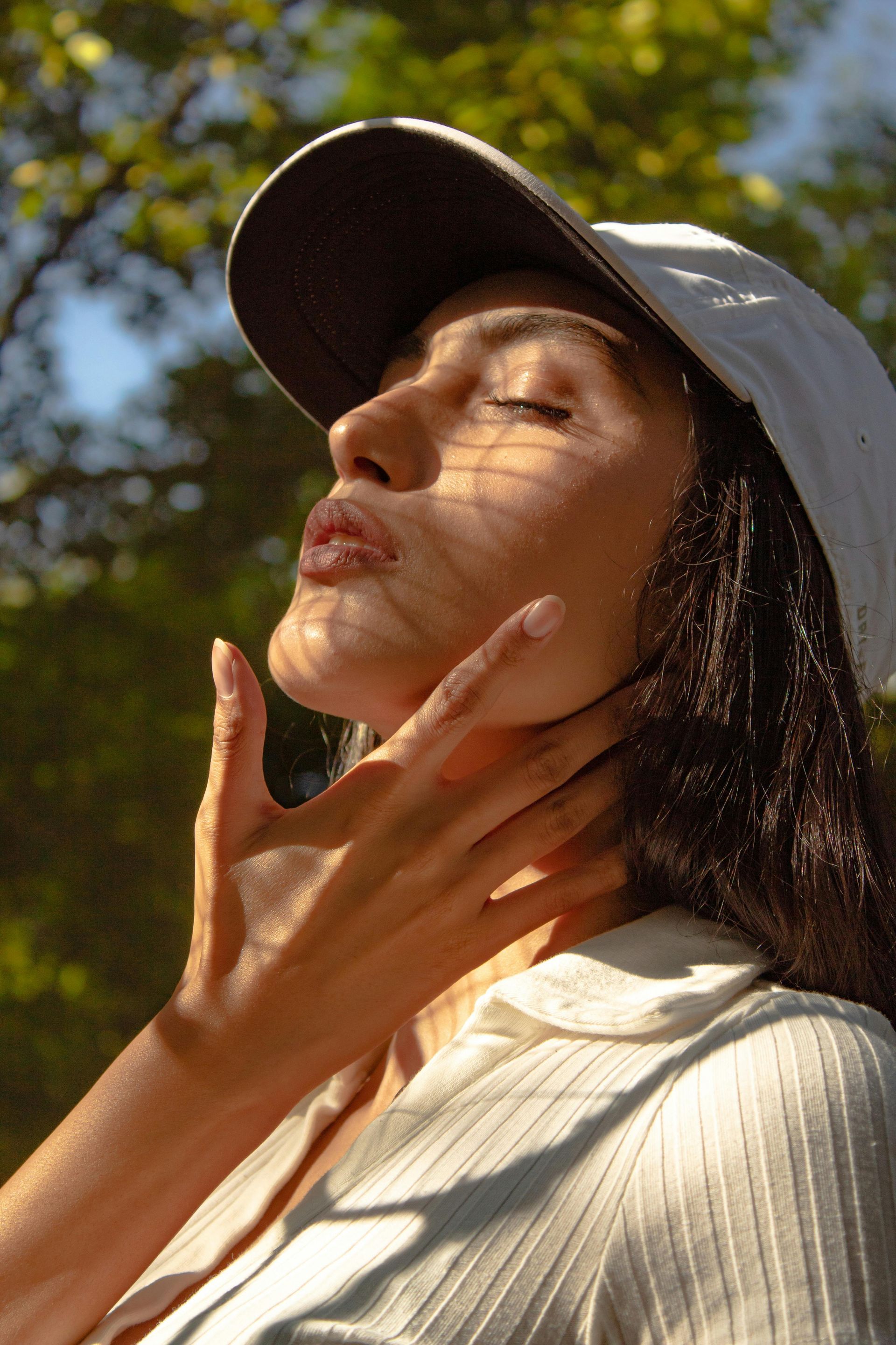 A woman in a baseball cap closing her eyes wither face towards the sun
