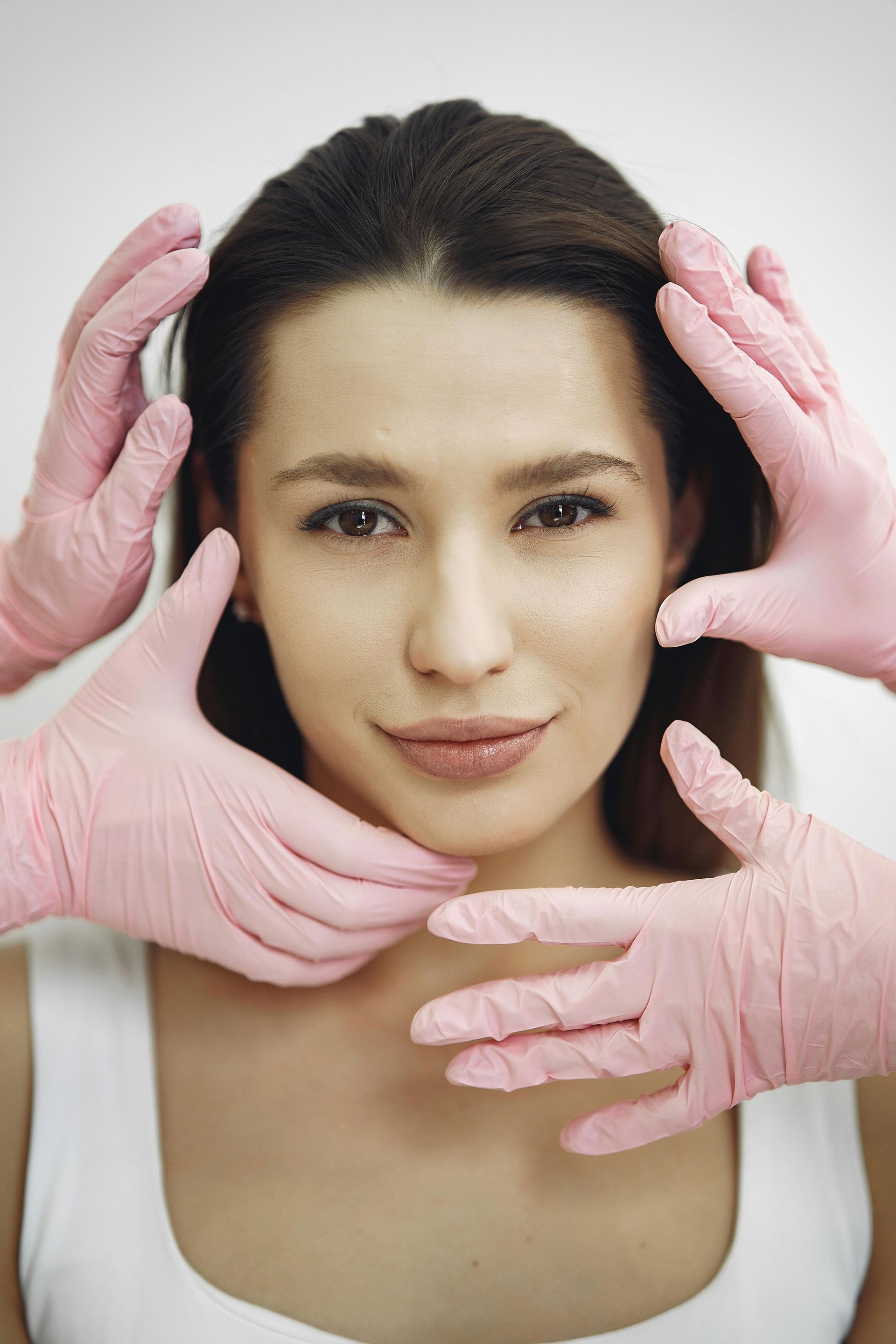 A woman posing, looking at camera, while gloved hands frame her face.