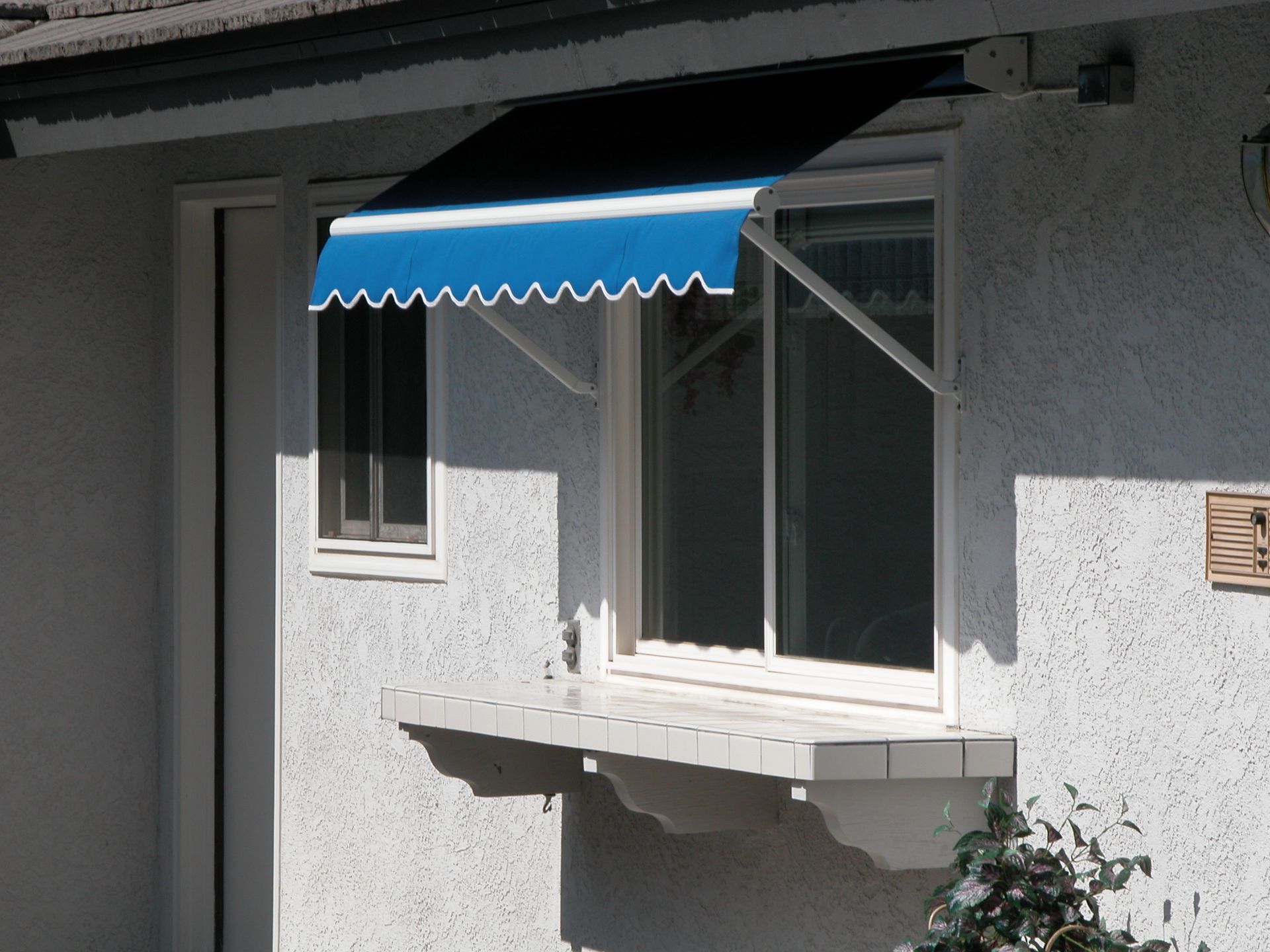 A white house with a blue awning over a window