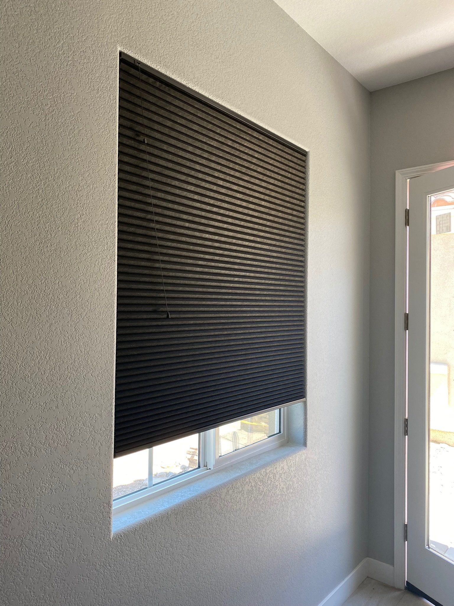 A window with a black blind on it in a room next to a door.