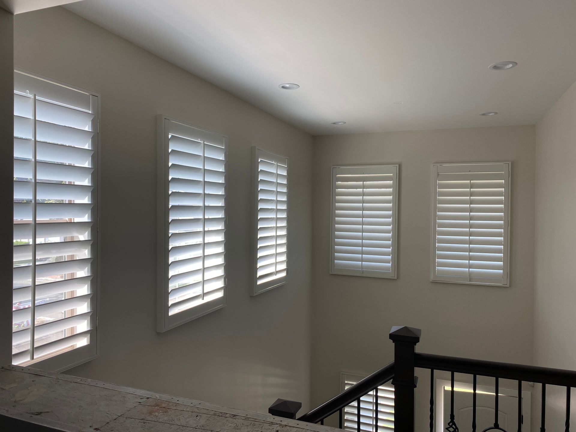 A room with white shutters on the windows and a black railing