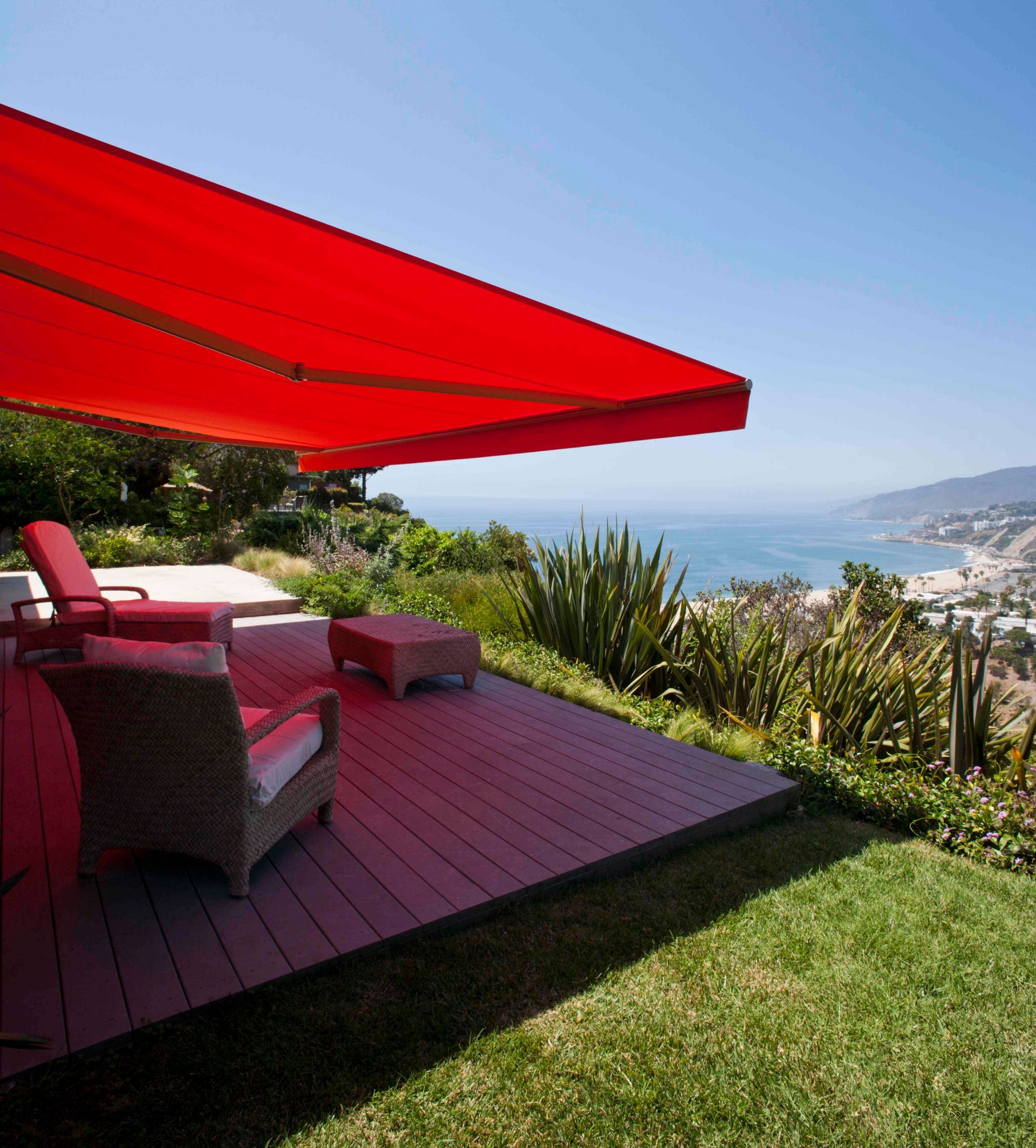 A red awning is covering a patio with chairs and a view of the ocean.