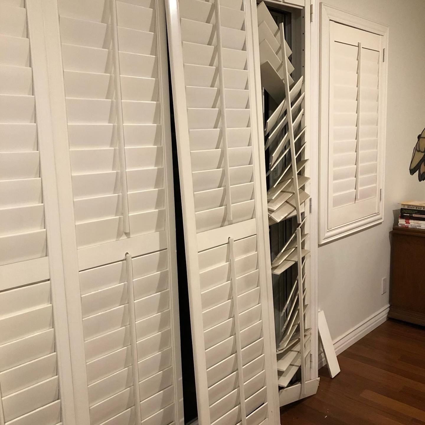 A room with white shutters on the doors and a wooden floor.