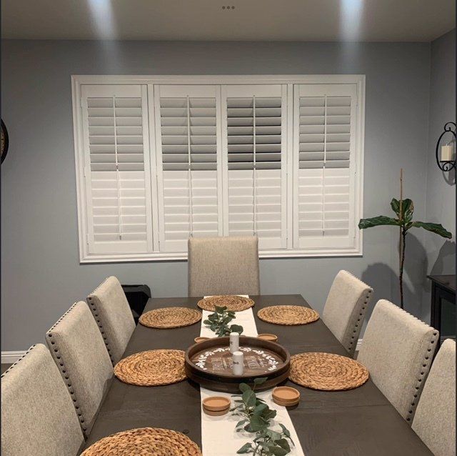 A dining room with a table and chairs and shutters on the windows