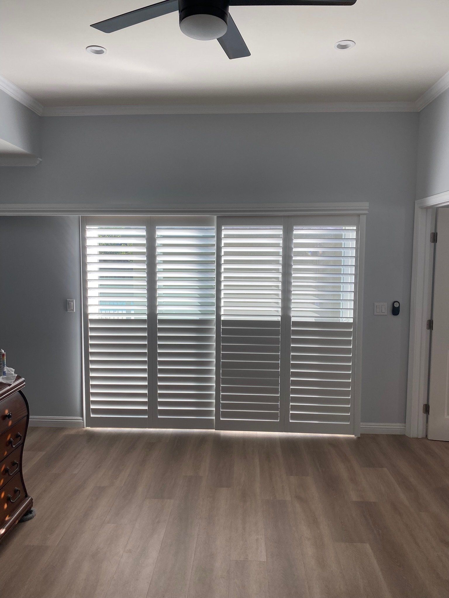 A living room with sliding glass doors and shutters and a ceiling fan
