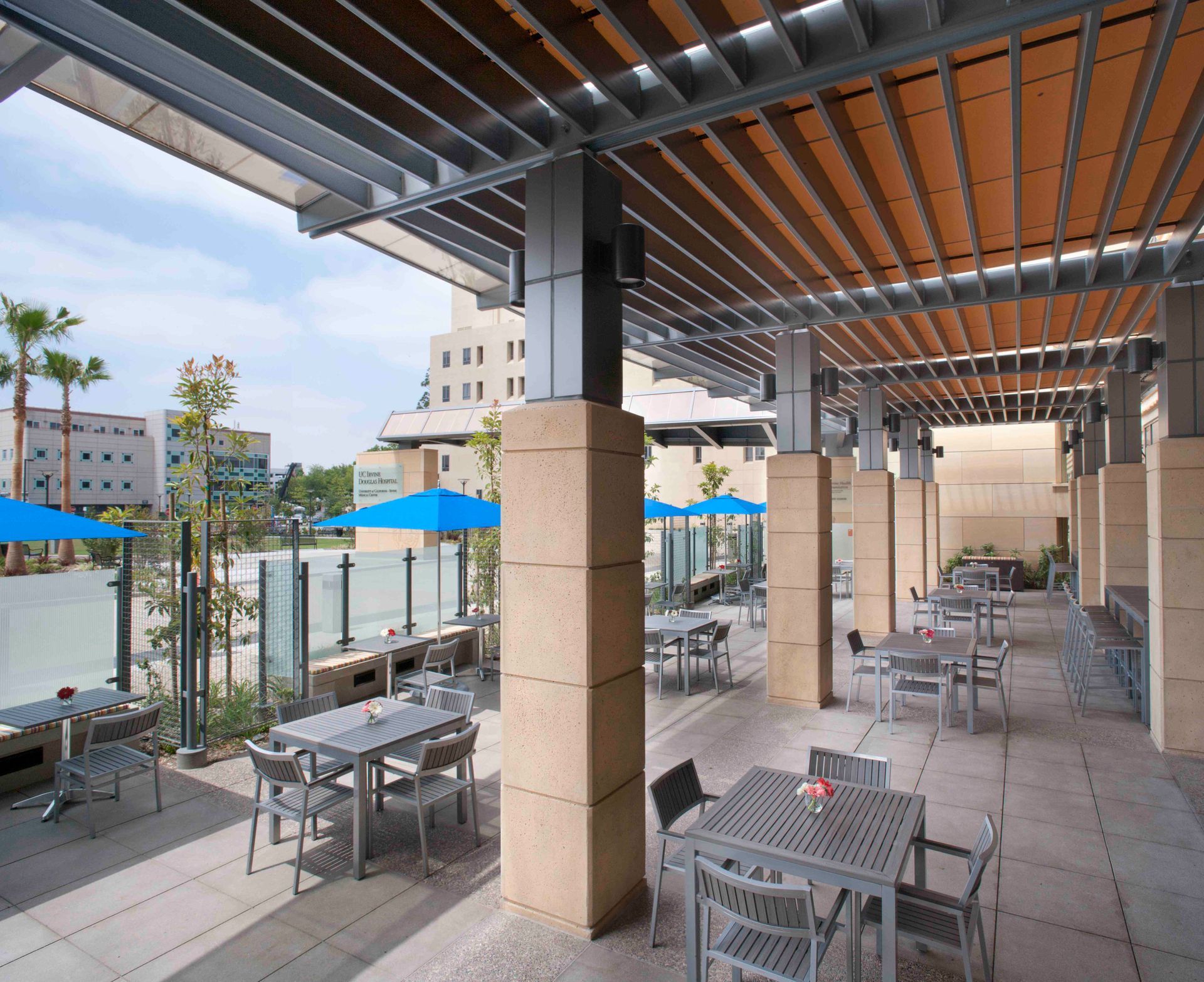 Tables and chairs under a pergola with blue umbrellas