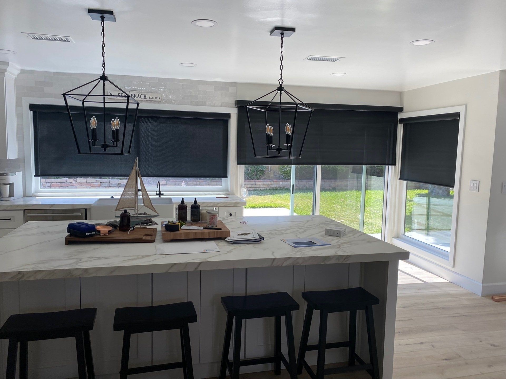 A kitchen with a large island and black blinds on the windows.